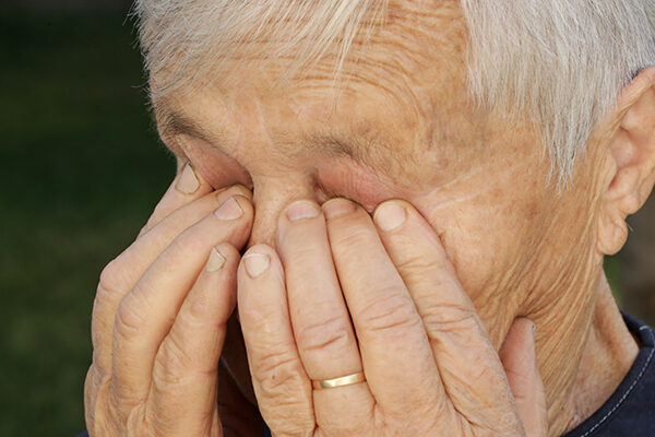 An older adult is rubbing their red eyes caused by dry eye syndrome.