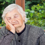 An older woman with white hair wearing a black and white polka dot sweater and black shirt. She is sitting with her elbow on a table, hand on her cheek, as she battles heart failure fatigue.