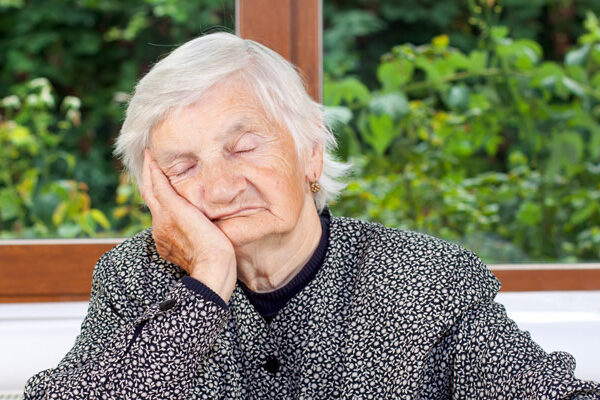 An older woman with white hair wearing a black and white polka dot sweater and black shirt. She is sitting with her elbow on a table, hand on her cheek, as she battles heart failure fatigue.