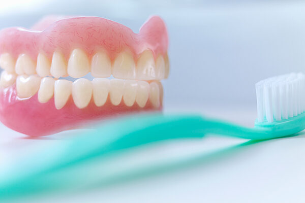 Dentures sitting on a white table with a teal A pair of dentures are sitting on a white table with a teal toothbrush in front of them.